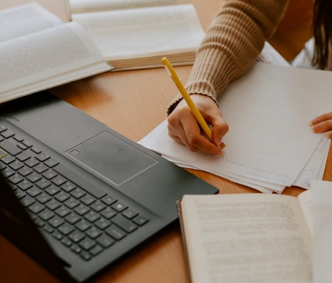 Photo of a desk showing a laptop and someone writing on paper